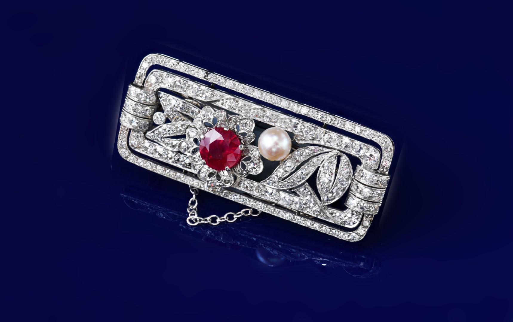 An Art Deco platinum brooch set with a round cut ruby of approximately 1.2ct, a natural pearl (5mm) and round cut diamonds, 12g, 4.3 x 1.9cm